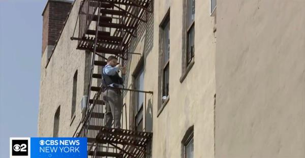 A man standing on a fire escape outside a Bronx building, investigating the circumstances of a 10-year-old girl's fall.