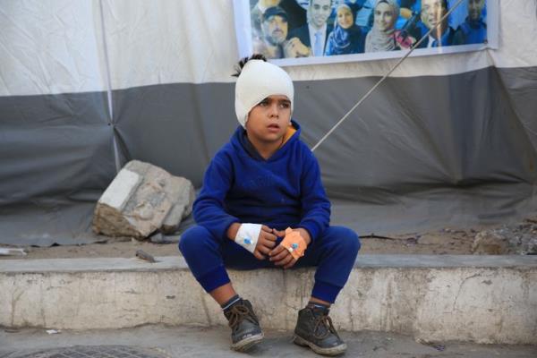 A Palestinian boy whose head is bandaged with an IV in his hands sits on the sidewalk outside Al-Ahli Baptist Hospital after an Israeli attack on northern Gaza's Jabalia camp, on Oct. 19, 2024.