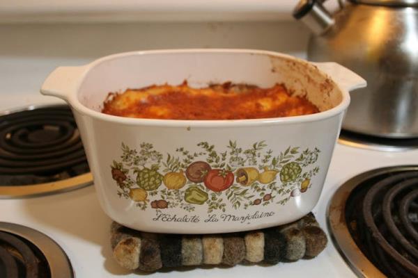 A pretty casserole dish filled with lasagne sits on a stove.