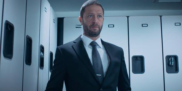 Richie from The Bear, played by actor Ebon Moss-Bachrach, is in a locker room wearing a dark, well-fitting suit and staring off-screen.